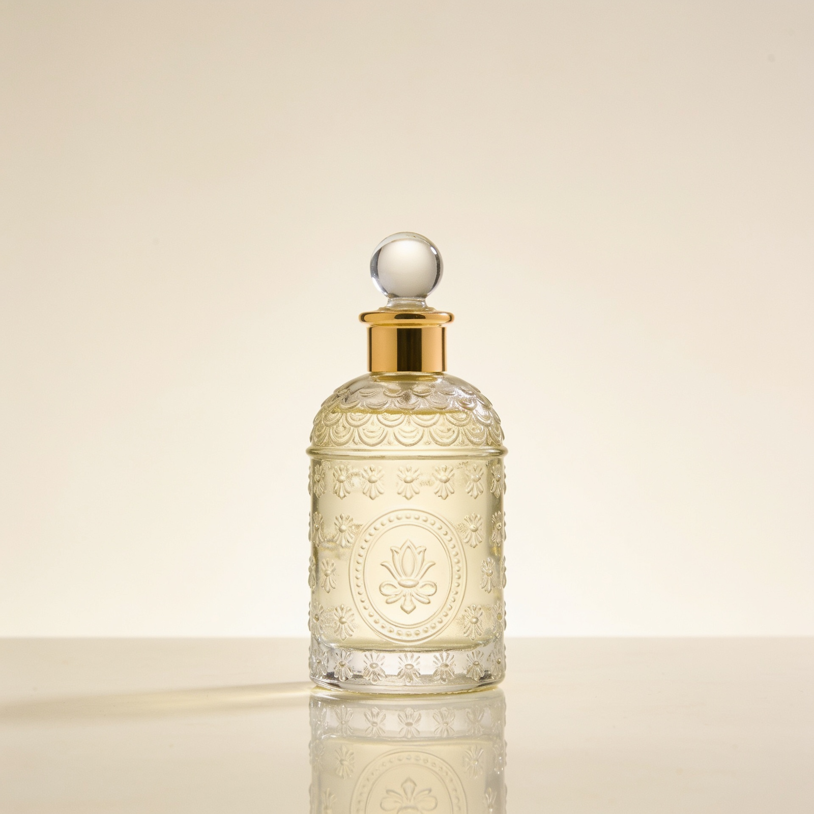 An ornate apothecary-style perfume bottle with intricate embossed floral decoration and a round crystal stopper, on a soft cream background